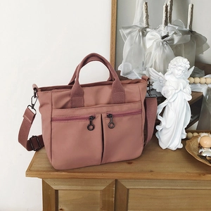 Detail of dusty rose nylon shoulder bag with circular zip pulls and reinforced handle