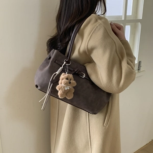 Detail of dark brown suede tote bag featuring slim straps and a cute plush bear charm