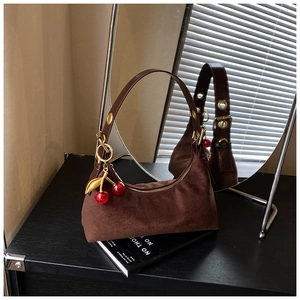 Detail of dark brown suede half-moon tote bag with decorative red cherry charms