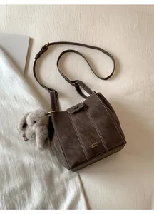 Detail of vintage dark brown bucket bag with plush elephant charm and golden logo on white fabric