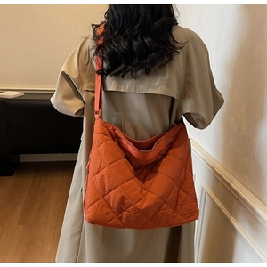 Detail of a bright orange quilted tote bag with diamond stitching and adjustable strap