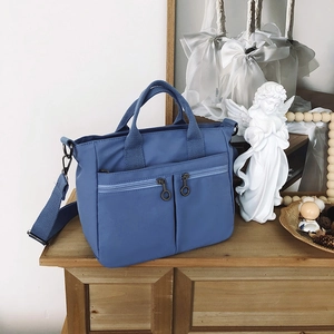 Blue nylon tote bag detail with double front zipper pockets on a wooden cabinet