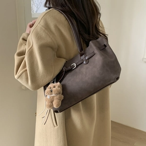 Detail of dark brown leather tote bag with decorative buckle strap and plush bear charm