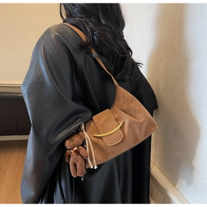 Close-up of brown faux leather dumpling bag with golden buckle and plush bear charm