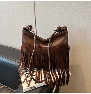 Dettaglio borsa a secchiello vintage marrone con frange e nappe su un divano