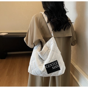 Detail of white quilted nylon tote bag with black Gentle Man label worn by model