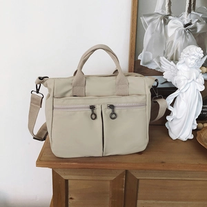 Detail of beige nylon tote bag with dual front zippers and vintage metal rings