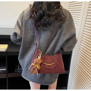 Detail view of a burgundy dumpling bag with a bear charm and gold buckle on a model