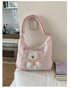 Détail du sac hobo rose matelassé en cœurs avec écusson de chiot sur canapé blanc