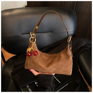 Detail of brown suede crescent bag with red cherry charm and adjustable leather strap
