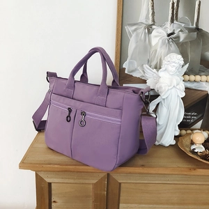 Detail of purple nylon tote bag featuring dual front zipper pockets and woven handles