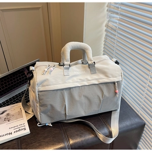 Détail d'un sac de sport gris avec poche zippée latérale et logo posé sur un banc en cuir