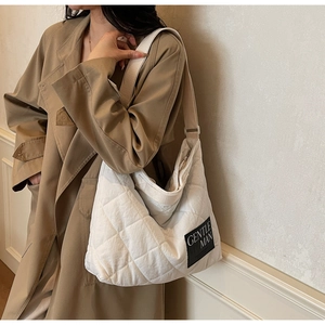 Detail of white quilted tote bag featuring a black Gentle Man label and wide shoulder strap