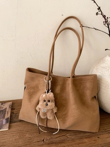 Brown vintage matte leather tote bag with long straps and plush charm on wooden table