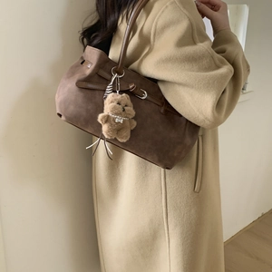 Detail of brown suede tote bag featuring a plush bear charm and elegant silver buckle