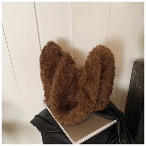 Close-up of fluffy brown faux fur bucket bag placed on fashion books and leather jacket