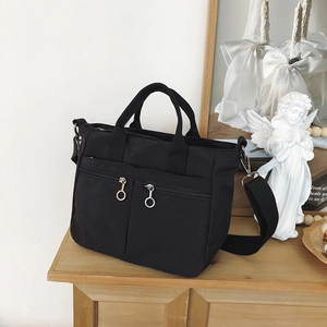 Detail of black nylon tote bag showing dual front zipper pockets with large metal pull rings