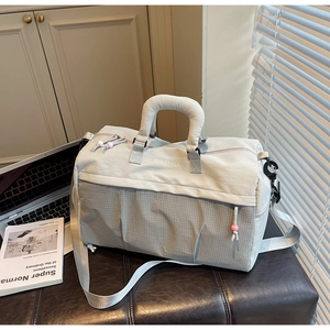 Détail du sac de voyage gris avec texture quadrillée, poignées rembourrées et logo brodé
