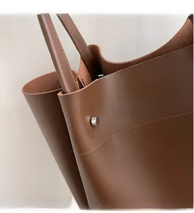 Close-up of brown leather tote bag handles with polished hardware and fine stitching