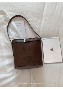 Détail d'un sac seau en daim marron foncé avec bandoulière sur surface texturée