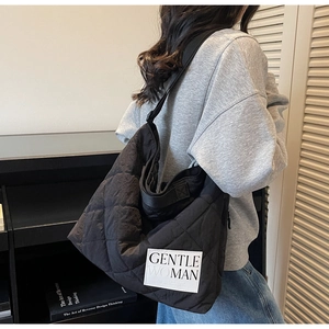 Detailed view of black quilted tote bag with GENTLE WOMAN label worn by casual model