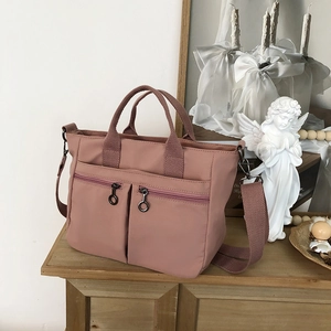 Detail view of pink waterproof nylon tote bag showing front zip pockets and wide straps
