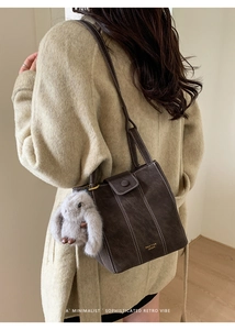 Close-up of retro brown bucket bag with white stitching and plush rabbit pendant detail