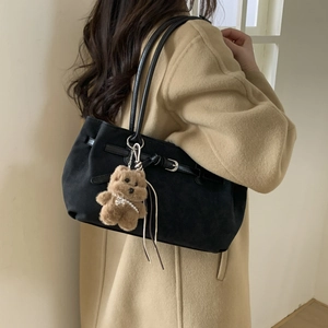 Close-up of black tote bag with brown plush bear charm on camel wool coat