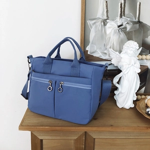 Detailed view of a navy blue nylon crossbody bag with dual zip pockets and woven handles