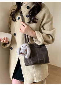 Detail of dark brown suede bucket bag with contrast stitching and rabbit plush charm