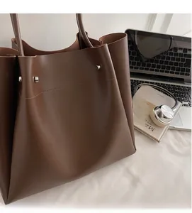 Detail of dark brown leather tote bag with silver rivets and minimalist commuter design