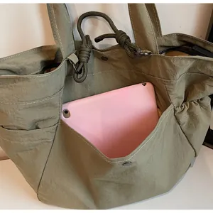 Detail view of olive green nylon tote bag featuring a large front pocket for tablet storage