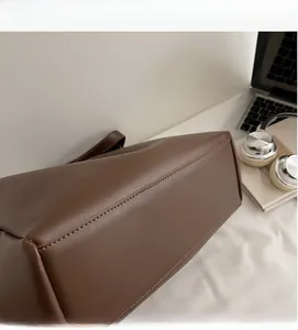 Detail view of large brown leather tote bag with sturdy base and smooth stitching