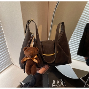 Detail of dark brown suede crescent bag with gold metal trim and cute plush bear charm