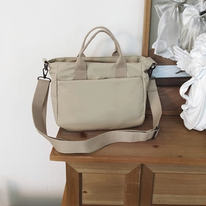 Detail of beige nylon tote bag featuring front pocket and adjustable woven shoulder strap