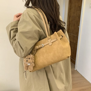 Detail view of large camel suede tote bag with puppy charm on a khaki trench coat
