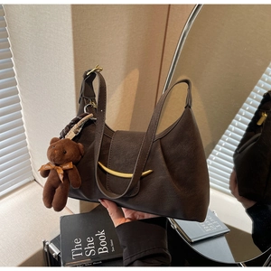 Detail of dark brown leather shoulder bag with gold clasp and plush bear charm