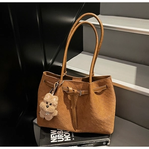 Detail der braunen geflochtenen Kunstledertasche mit einem Plüsch-Hundeanhänger