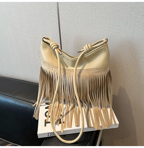 Dettaglio di una borsa a secchiello crema con frange decorative e tracolla in corda annodata