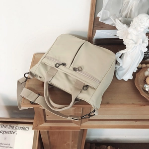 Detail of a beige nylon tote bag with functional zippers on a vintage wood background