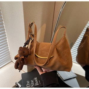 Detail of caramel leather dumpling bag with golden clasp and cute bear charm accent