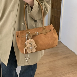 Detail of caramel brown suede tote with metal buckle strap and plush bear charm decoration