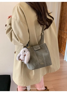 Detail of grey-green bucket bag with plush rabbit charm and gold logo on long coat