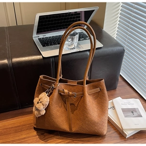 Detailaufnahme der braunen geflochtenen Ledertasche mit Bärenanhänger im Büro-Stil