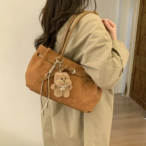 Brown oversized tote bag in matte faux leather with plush bear charm on beige coat