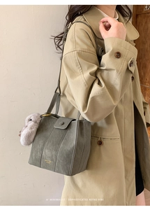Detail of vintage grey bucket bag with plush rabbit pendant on beige trench coat