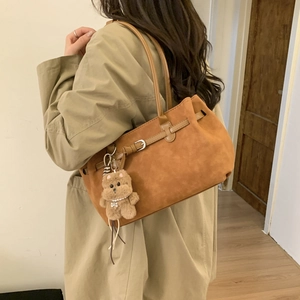 Close-up of brown suede tote bag with a cute plush bear charm on a trench coat model