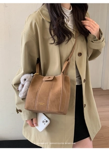 Brown suede bucket bag with fine stitching, gold logo, and a plush lamb keychain detail