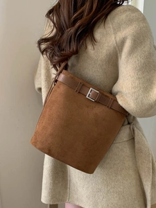 Sac seau minimaliste en daim marron foncé avec bandoulière réglable sur manteau