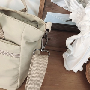 Close-up of durable metal hook and D-ring attachment on the beige nylon shoulder bag
